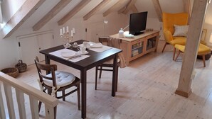 Une pièce mansardée chaleureuse, avec une table en bois, des chaises, un téléviseur et un fauteuil jaune.