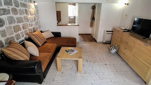 Un salon avec un mur en pierre, des poutres apparentes, un canapé marron, une table basse en bois et un meuble pour la télévision.
