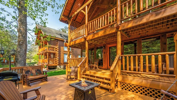 A wooden cabin with a deck, outdoor seating, and a fire pit. - Creekside Dreams – Hot Tub, Fire Pit, Pool Table, 2 Bunk Beds & Creekside Deck (Pigeon Forge)