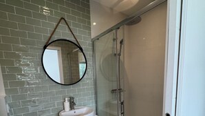 A modern bathroom with a white sink, a round mirror, and a glass-enclosed shower. - Cosy studio in quiet location, Questembert town center (Questembert)