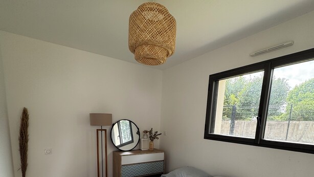 A bedroom with a bed, a bedside table, a lamp, a window, and a hanging light fixture. - Cosy studio in quiet location, Questembert town center (Questembert)