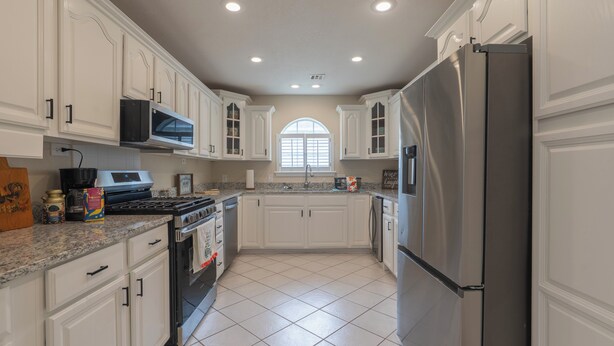 A kitchen with white cabinets, stainless steel appliances, and a tiled floor.
