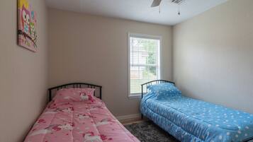 A bedroom with two beds, one pink and one blue, and a window with blinds.