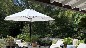 Een terras buiten met een tafel en stoelen, omringd door potplanten en een overdekte zithoek.
