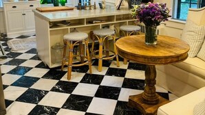 Een keuken met een geruit vloertje, een centraal eiland met krukken, en een ronde houten tafel met een bloevas.