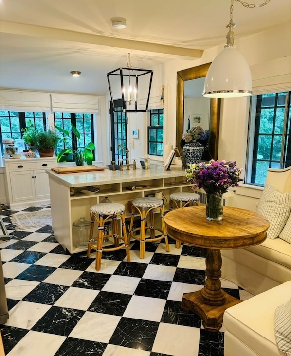 A kitchen with a checkered floor, a central island with stools, and a round wooden table with a vase of flowers.