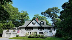 Een groot, twee verdiepingen hoog huis met een steile zadeldak, een veranda en een garage met een Amerikaanse vlag.