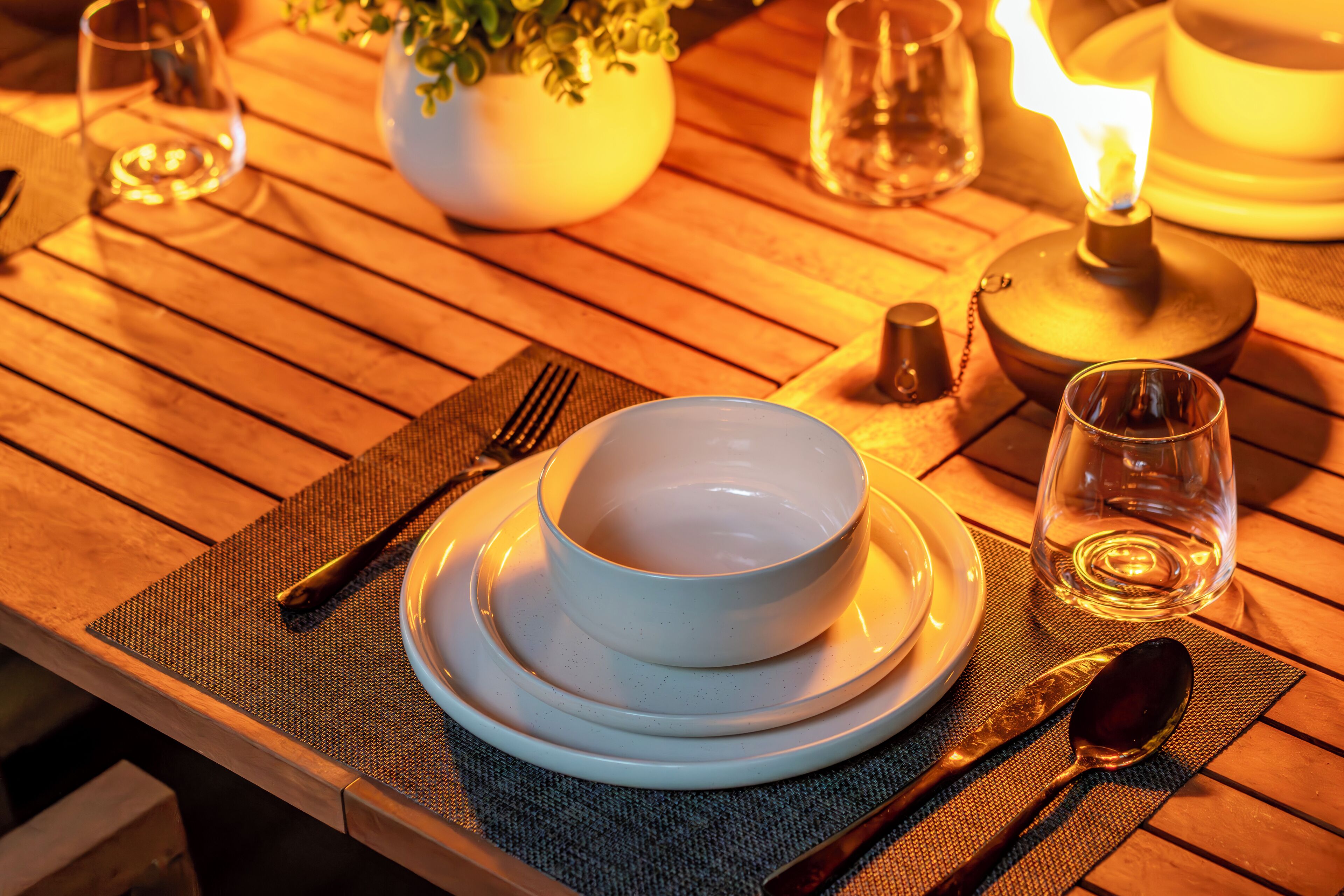 A wooden table set with white plates, bowls, cutlery, and a lit candle.