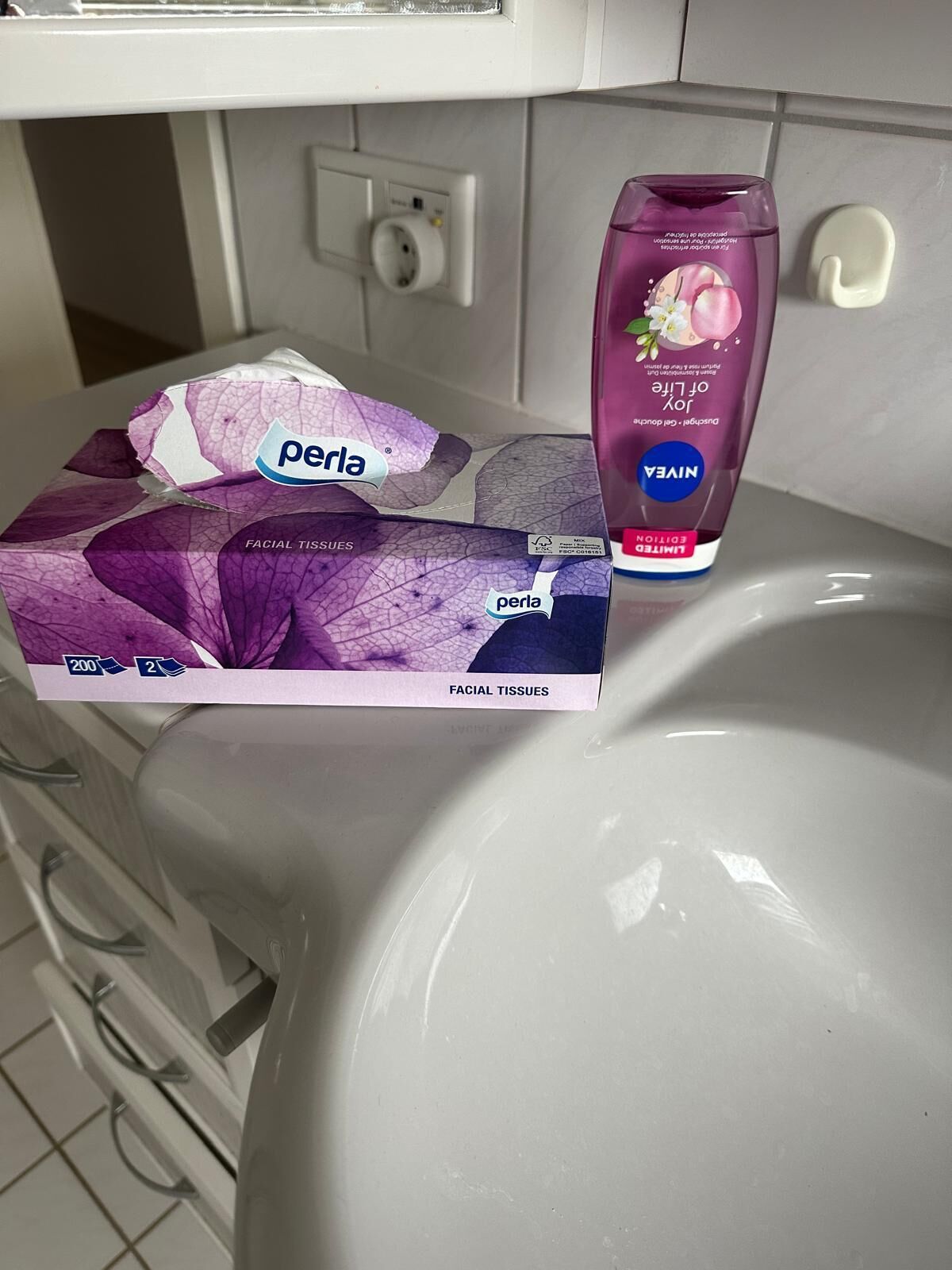 Une boîte de mouchoirs Perla et un flacon de lotion Nivea sur le lavabo d’une salle de bain.