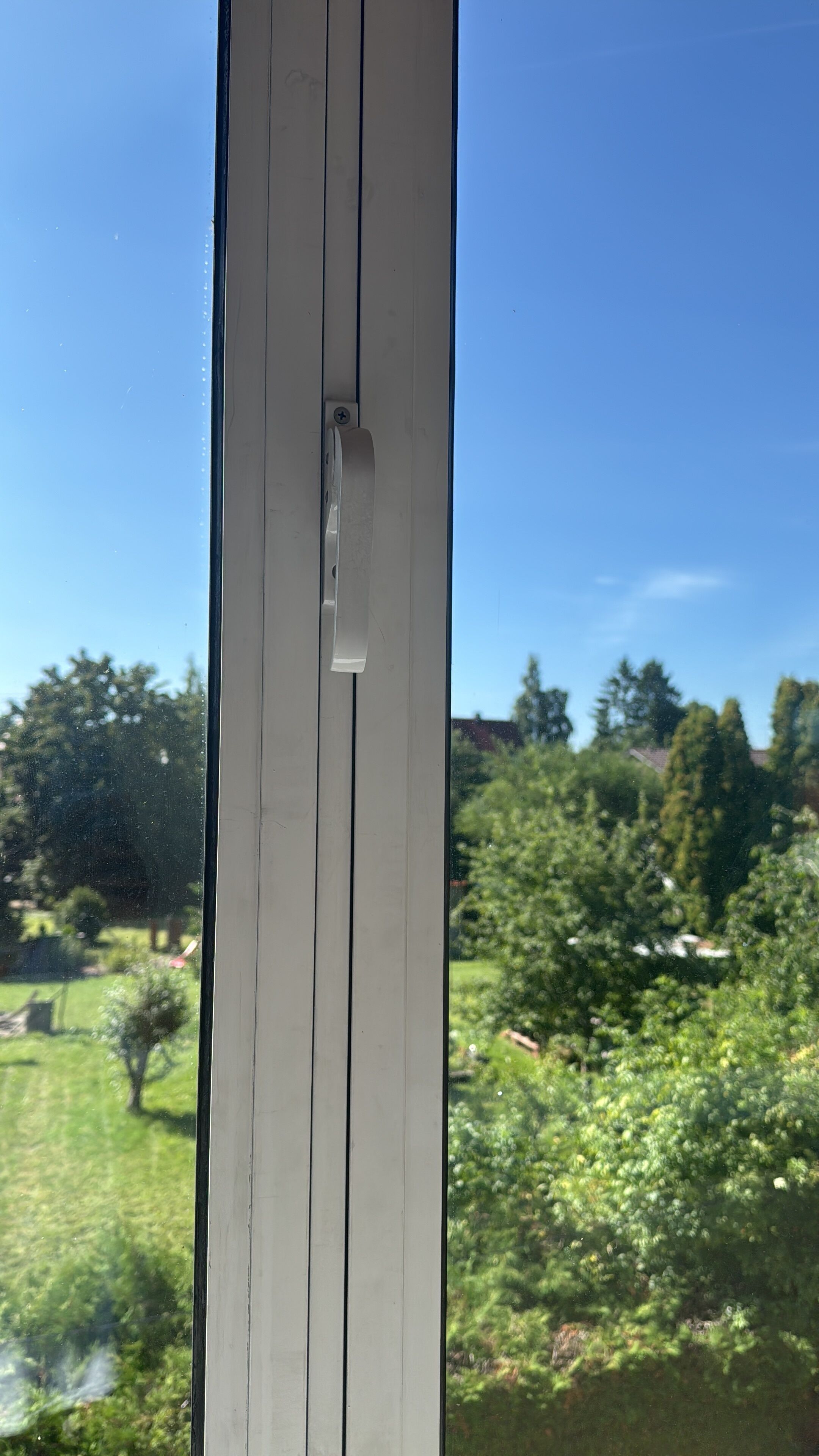 Een raam met uitzicht op een groen landschap, met bomen en een gebouw in de verte.