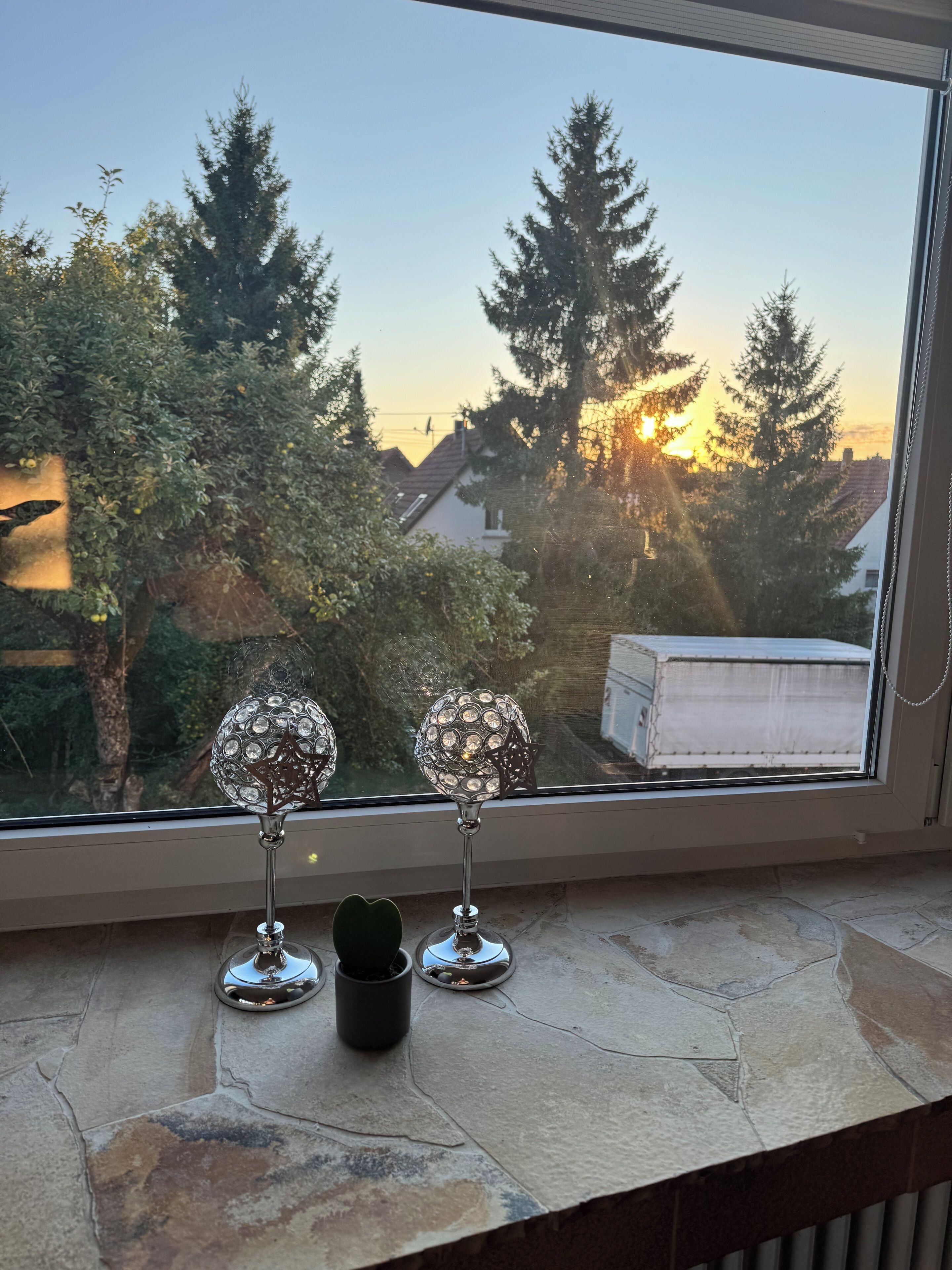 A window with a view of trees and a sunset.