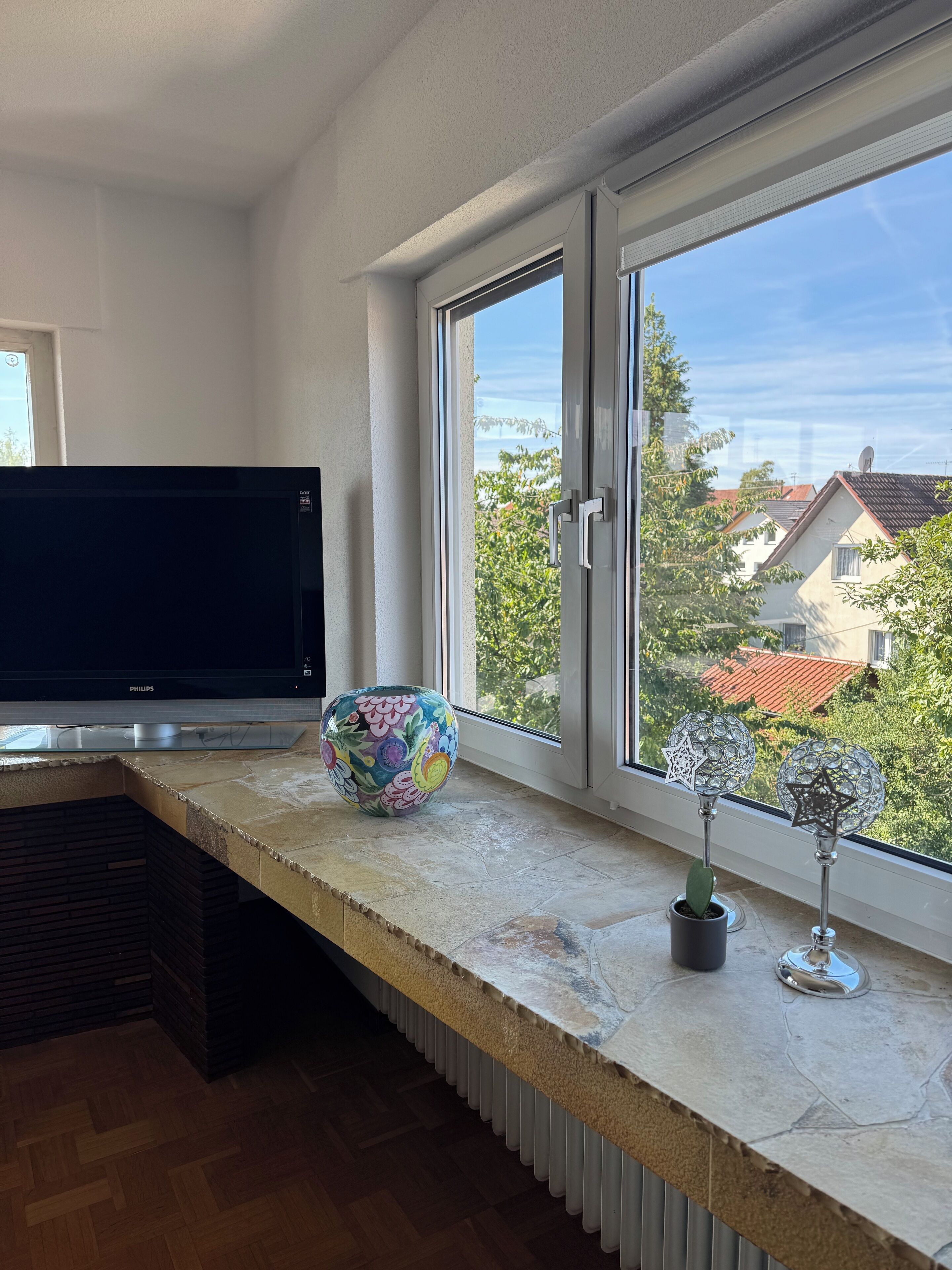 Een moderne keuken met een groot raam, een flatscreen televisie, een decoratieve vaas en een potplant.