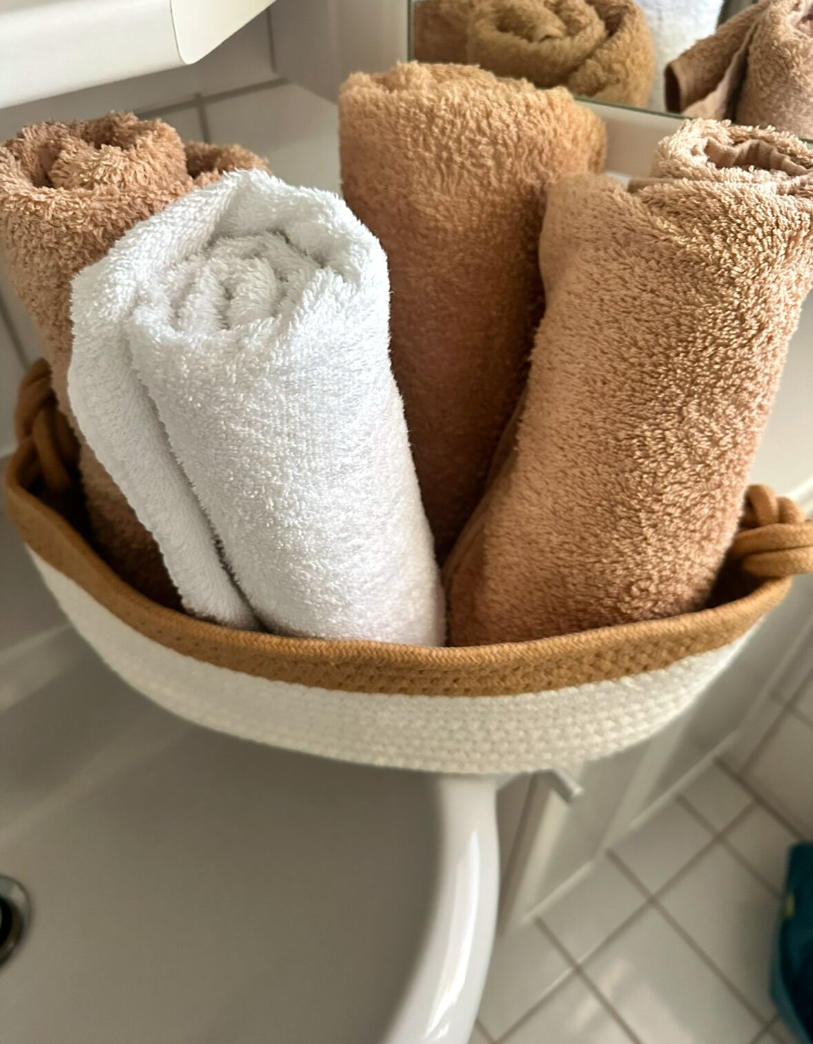 A white ceramic bowl filled with neatly folded towels in shades of brown and white.