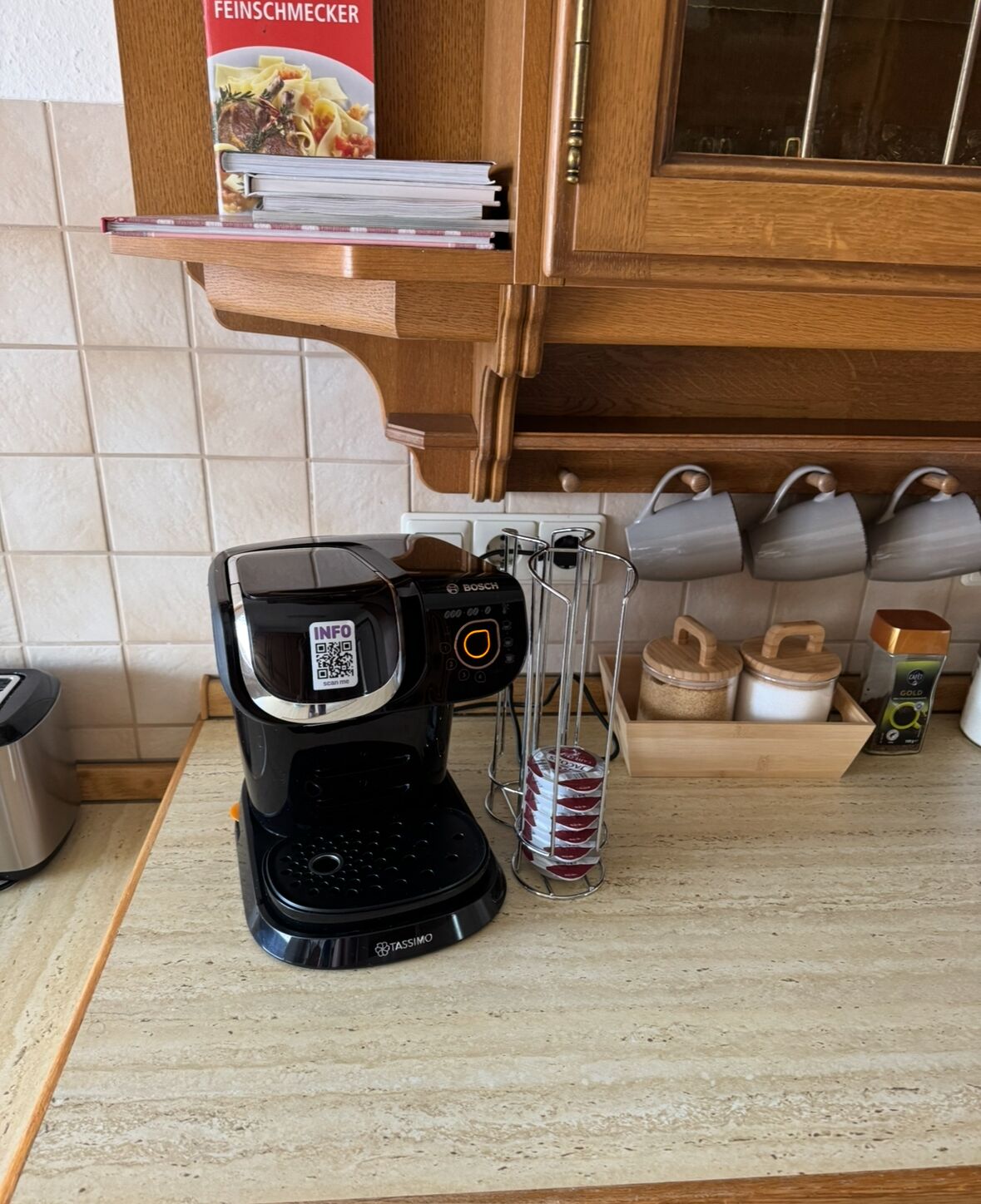 A kitchen with a coffee maker, a spice rack, and a cookbook on the shelf.