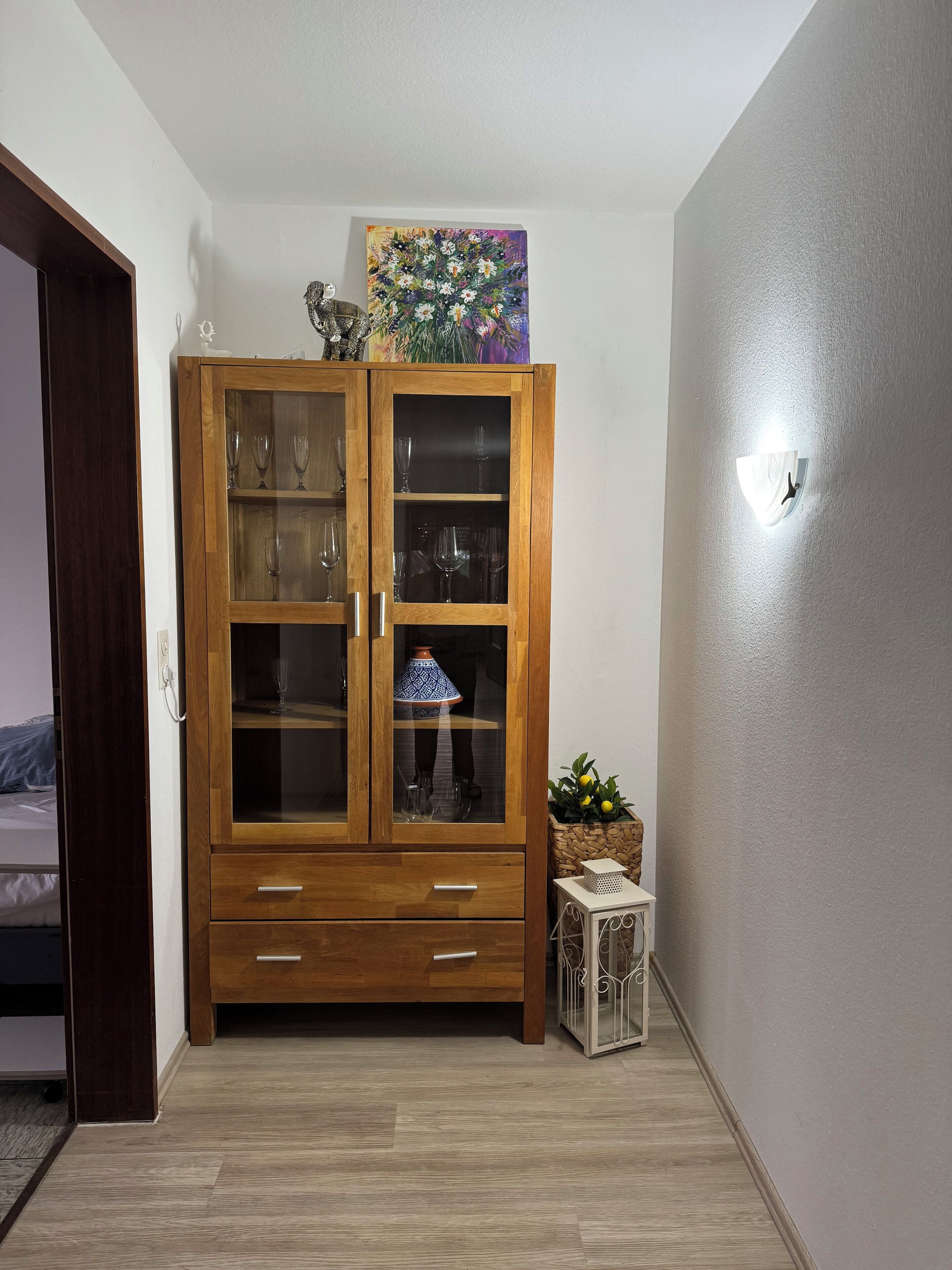 A wooden cabinet with glass doors, a small table with a lamp, and a painting on top.