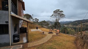 A building with a visible number '15' on the side, a paved pathway, picnic tables, and a large tree in the background. - Villa da Serra Suites (Lima Duarte)