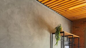 A modern interior with a concrete wall, a wooden desk, a black chair, and a hanging plant. - Villa da Serra Suites (Lima Duarte)