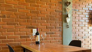 A brick wall, a wooden table with two black chairs, a bottle of wine, and decorative heart-shaped items on the wall. - Villa da Serra Suites (Lima Duarte)