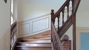 Eine Holztreppe mit Geländer, die zu einer Zwischenebene mit einer Tür und einem gerahmten Gemälde an der Wand führt.