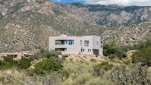 Un bâtiment moderne à deux étages, doté de grandes fenêtres, situé sur une colline avec une chaîne de montagnes en arrière-plan.