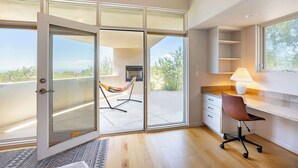 Une chambre moderne dotée d’une porte-fenêtre coulissante donnant sur un balcon, d’un bureau avec une chaise et d’une lampe.