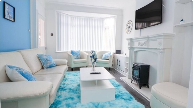 A living room with a white sofa, two armchairs, a coffee table, a fireplace, and a TV mounted on the wall. - LATE CHECK-OUT AVAILABLE<br>We offer a 20% discount for all stays of 28+ nights and 10% discount for all stays of 7+ nights. Discounted rate is automatically applied and includes all utility bills and bi-weekly professional cleaning. No hidden fees. (Anfield)