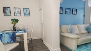 A dining area with a table set for two, a sofa, and a blue accent wall. - LATE CHECK-OUT AVAILABLE<br>We offer a 20% discount for all stays of 28+ nights and 10% discount for all stays of 7+ nights. Discounted rate is automatically applied and includes all utility bills and bi-weekly professional cleaning. No hidden fees. (Anfield)