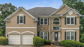 Une maison à deux étages avec une façade en pierre, deux portes de garage et une entrée principale dotée d’un petit porche.