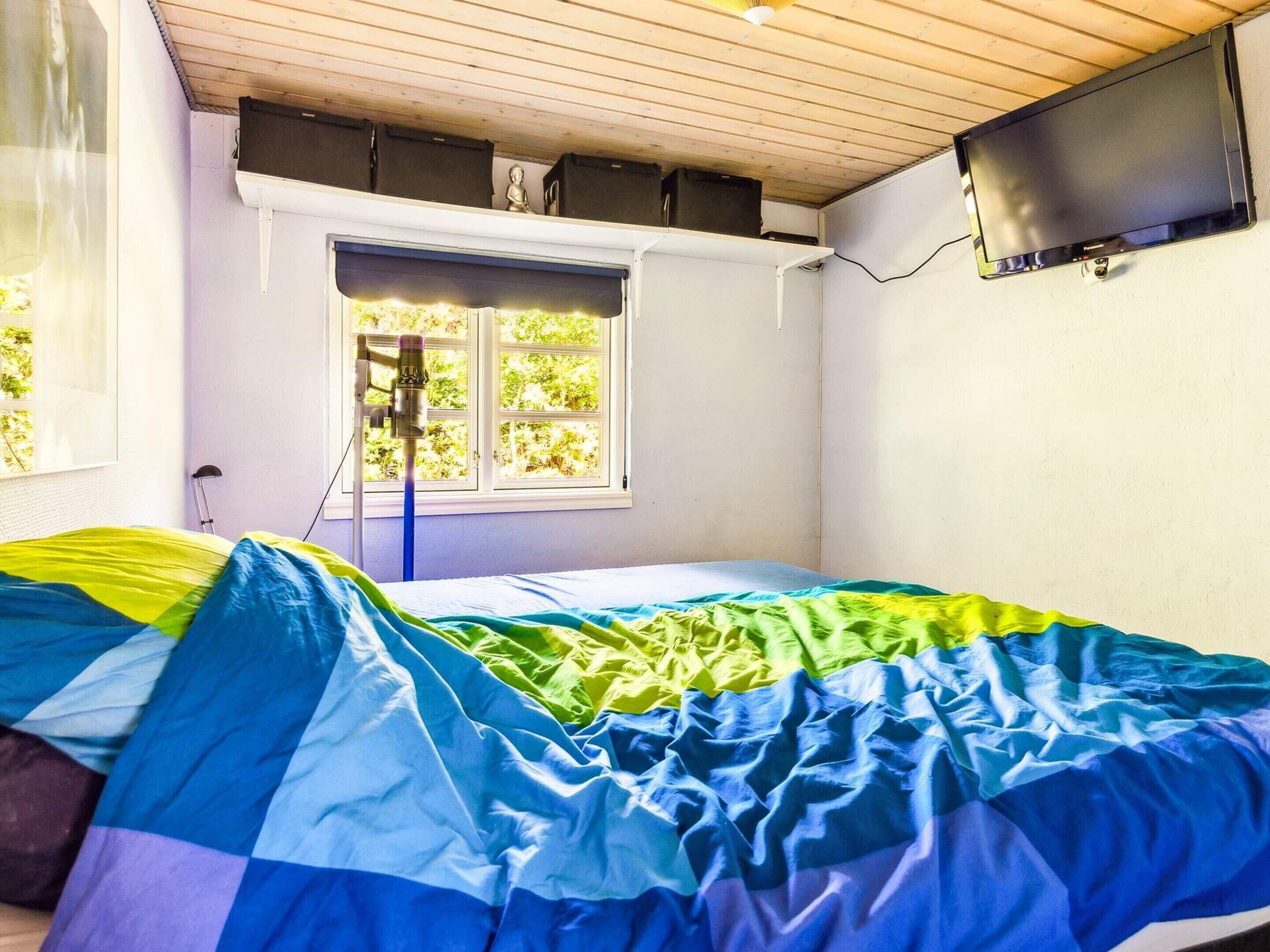 Ein Schlafzimmer mit Bett, Fenster, Deckenventilator und an der Wand montiertem Fernseher.