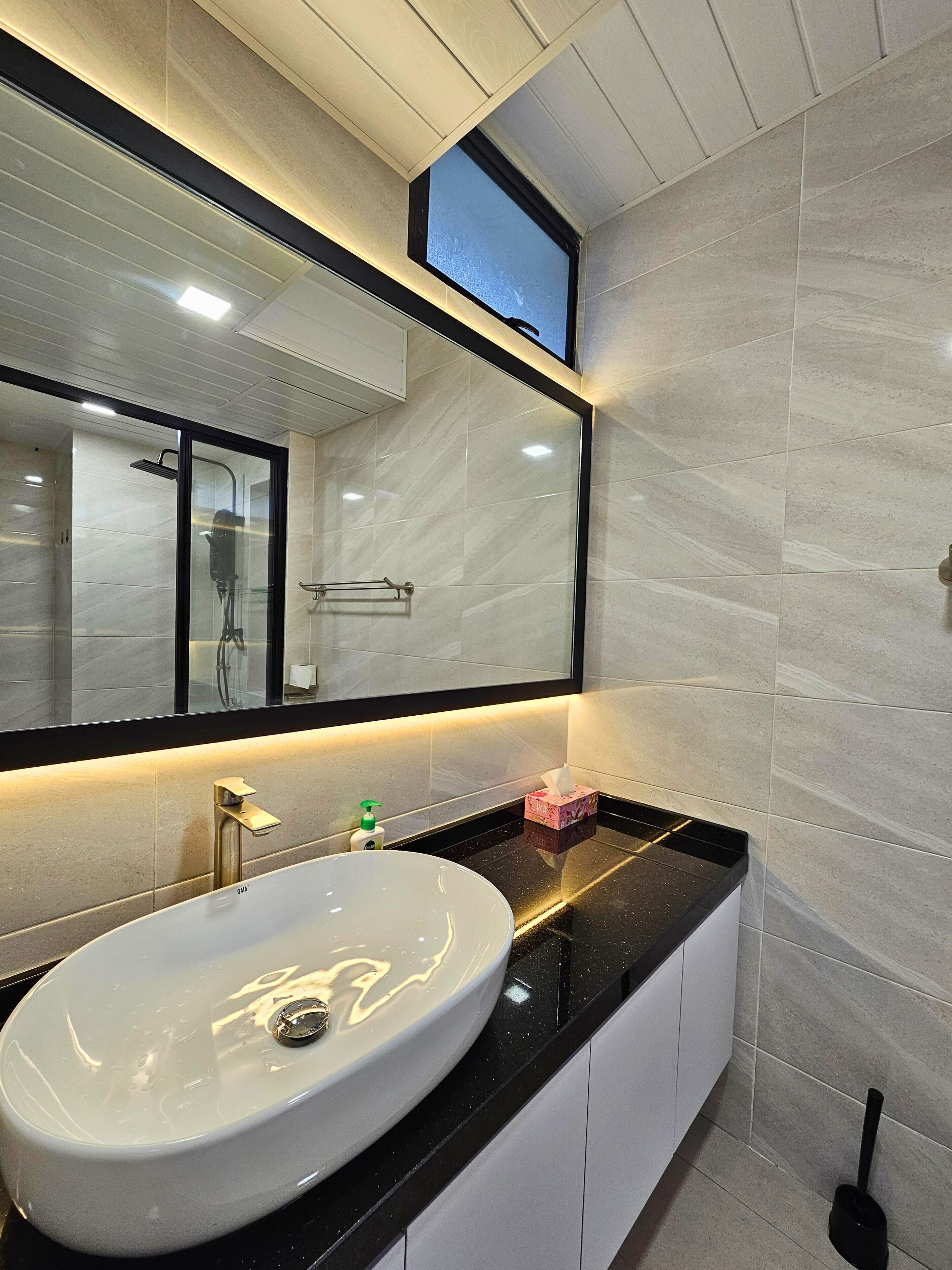 Un baño moderno con un lavamanos ovalado grande, un espejo y un cabezal de ducha de mano.