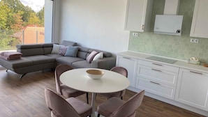 Une cuisine moderne avec des meubles blancs, un canapé gris et une table à manger ronde entourée de chaises.