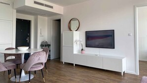 Un salon moderne comprenant un coin repas, des meubles blancs, un grand tableau et un miroir rond accroché au mur.
