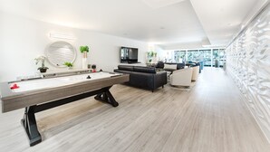 A modern living room with a pool table, a black leather sofa, and a flat-screen TV. - Waterfront Retreat—Views, Pool, Hot Tub, Gym Walk to Beach & Boca Resort! (Boca Raton)