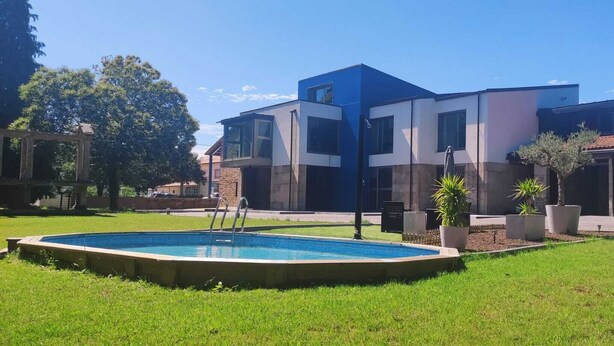 Un edificio moderno con piscina, rodeado de césped cuidado y plantas en macetas.