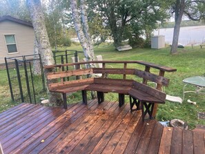A wooden deck with a bench, surrounded by trees and a grassy area.