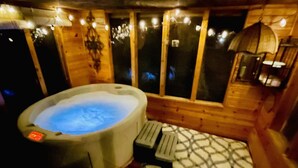 A hot tub in a wooden cabin with a patterned floor and a window with curtains. - Charming 2-bedroom cabin on lake near Duluth MN with Air Conditioning (Saginaw)