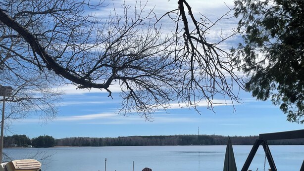 A lakeside deck with Adirondack chairs, a table, and a swing set. - Charming 2-bedroom cabin on lake near Duluth MN with Air Conditioning (Saginaw)