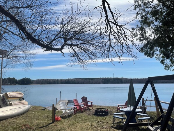 A lakeside deck with Adirondack chairs, a table, and a swing set.