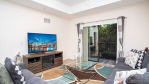 A living room with a flat-screen TV, a glass-top coffee table, grey sofas, and a patterned rug.