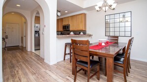 A dining area with a wooden table and chairs, a kitchen with wooden cabinets, and a chandelier.