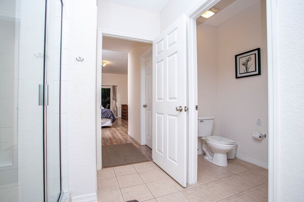 Une salle de bain comprenant des toilettes, une douche et une porte donnant sur une chambre.