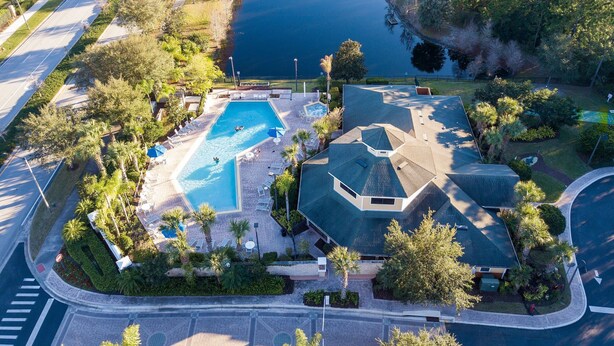 An aerial view of a residential area with a swimming pool, a tennis court, and a large house with a sloped roof.