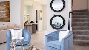 A modern living room with a sofa, two armchairs, a coffee table, and decorative items. There is a staircase leading to another level.