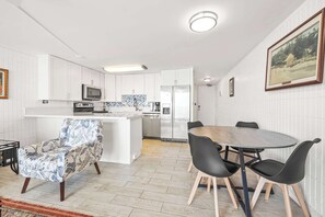 Une cuisine moderne avec des meubles blancs, un îlot central et un coin repas comprenant une table ronde et des chaises noires.