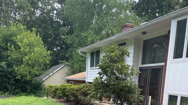 A residential property with a well-maintained garden, a curved driveway, and a house with large windows and a brick chimney.