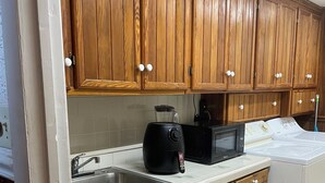 A kitchen with wooden cabinets, a sink, a microwave, and a trash bin.
