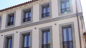Un edificio de varios pisos con fachada blanca, ventanas con marco azul y techo de tejas rojas.