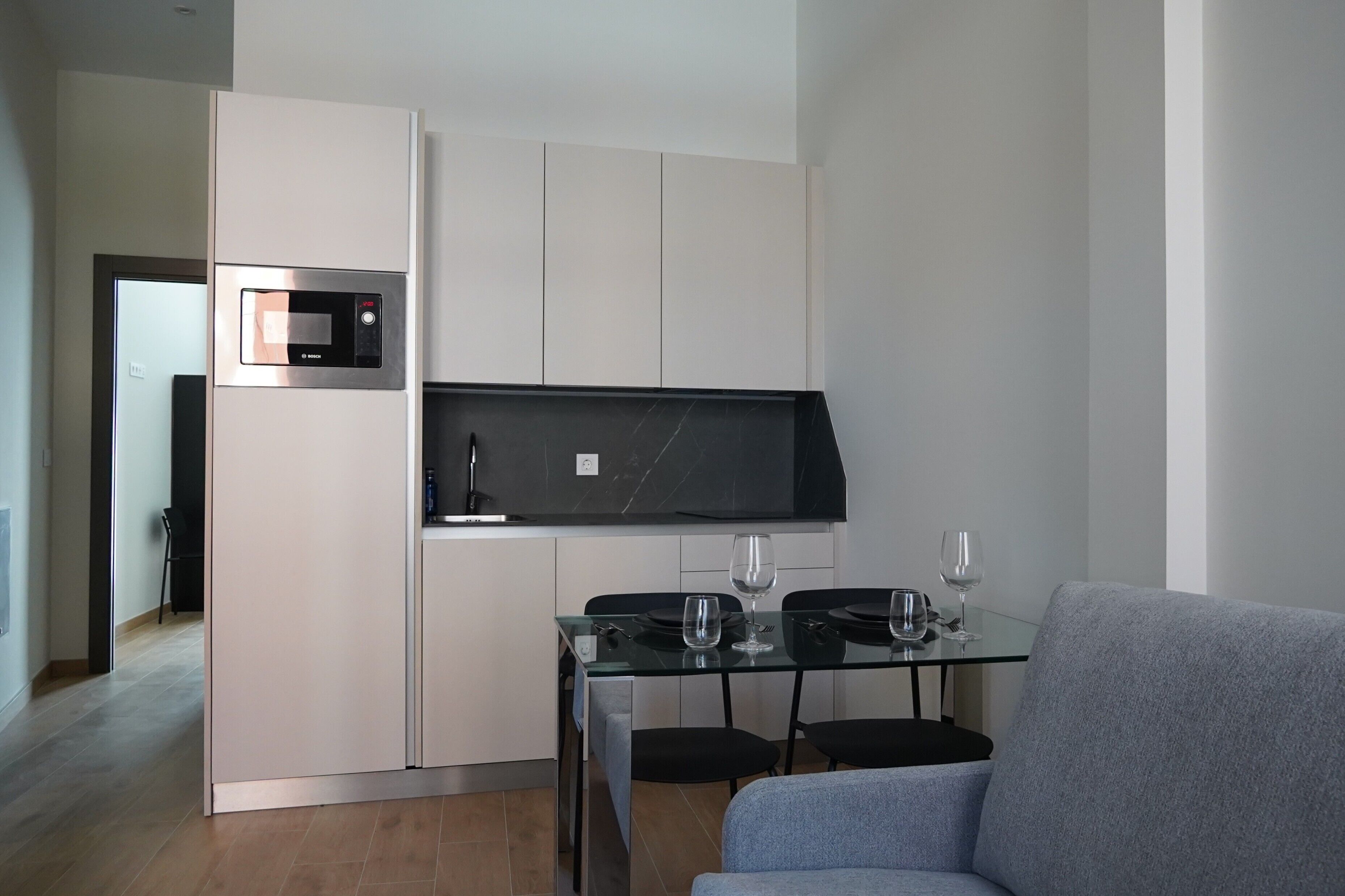 Une cuisine moderne dotée d’un four à micro-ondes encastré, d’un plan de travail noir et d’une table à manger en verre avec des chaises.