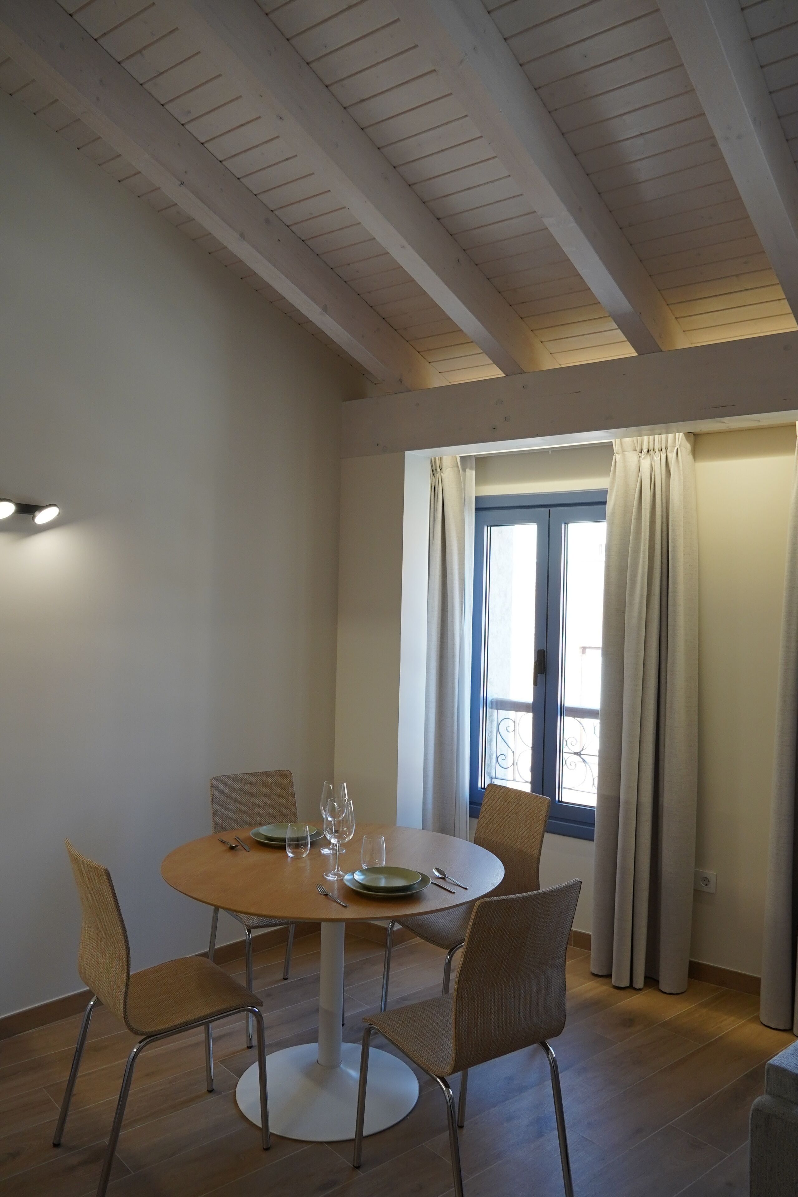 A dining area with a round table, four chairs, and a window with curtains.