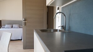 Una cocina moderna con pileta integrada y un dormitorio independiente con cama y mesita de noche.